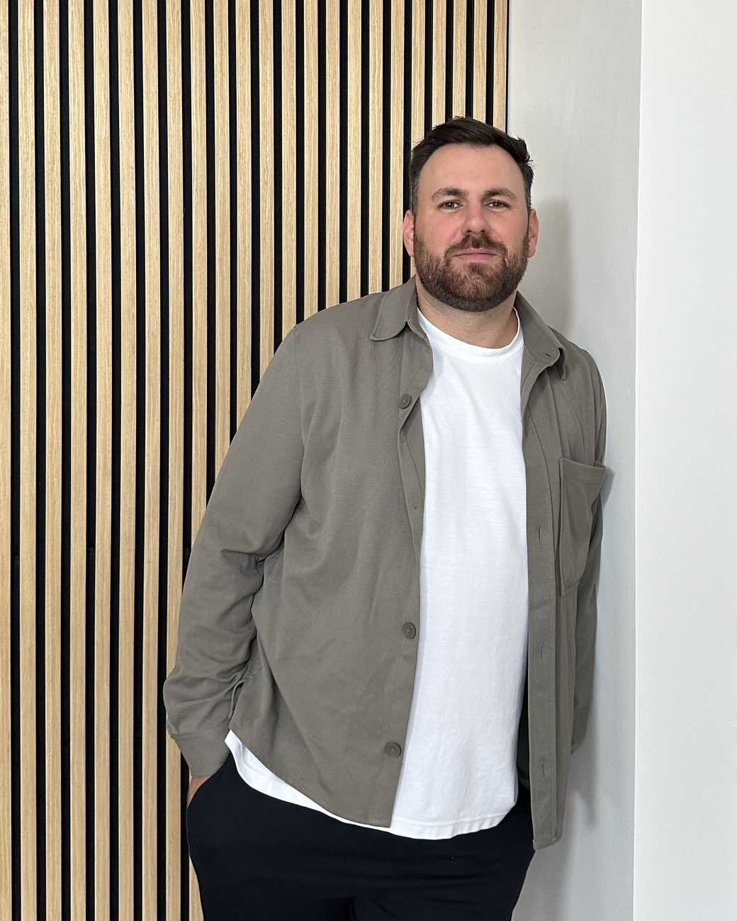 Oliver Klemm, Inhaber von 785 Media, lehnt lächelnd an einer Wand mit Holzlamellen